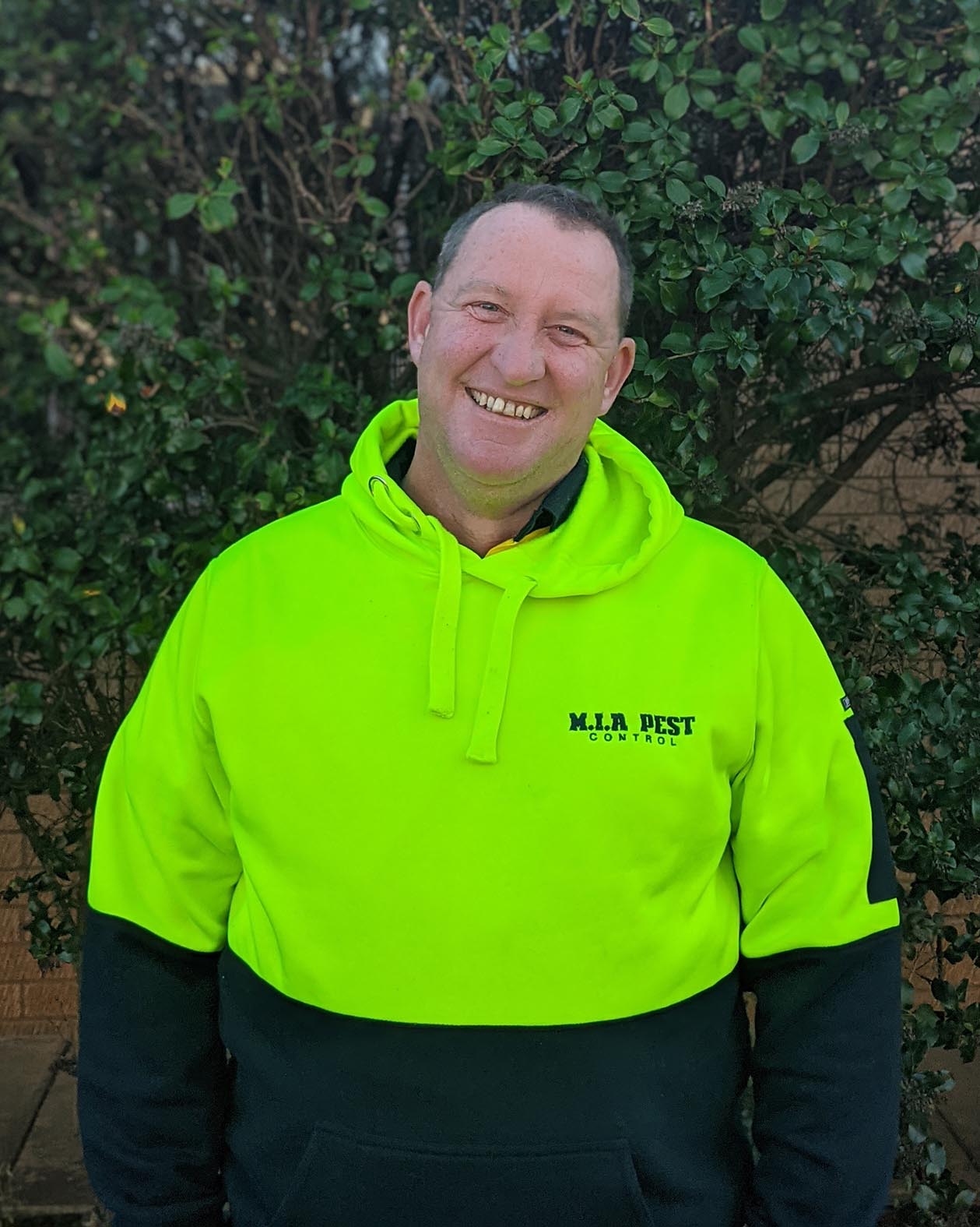 portrait photo of a man in high-vis fluro yellow with bush leaves as background, Scotty of MIA Pest Control Vermin Control extermination griffith nsw logo riverina murrambidgee irrigaiton area leeton